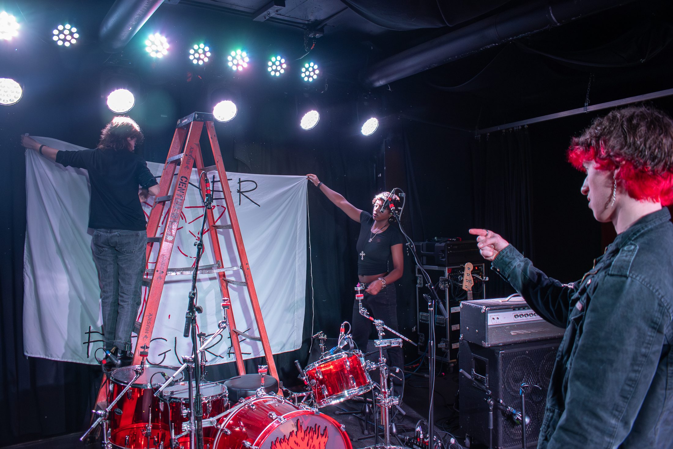 Ezi and Chris hang up their homemade Father Figure backdrop while Alex, from openerband Possums, stands back to be sure the backdrop is hung up straight.